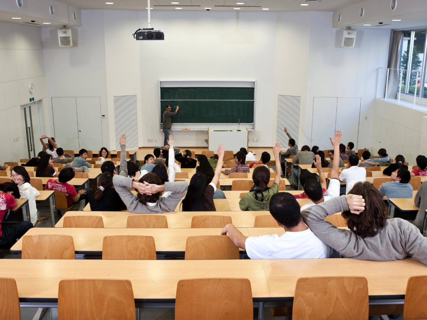 A full lecture hall with students raising their hands