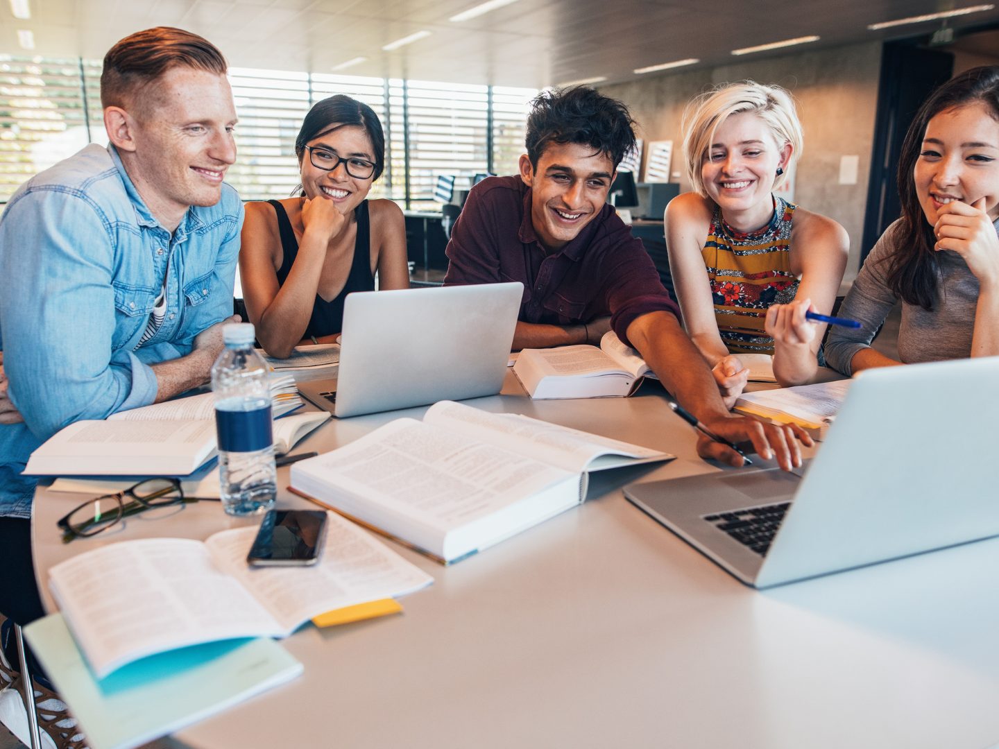 A group of students around a table with laptops and books